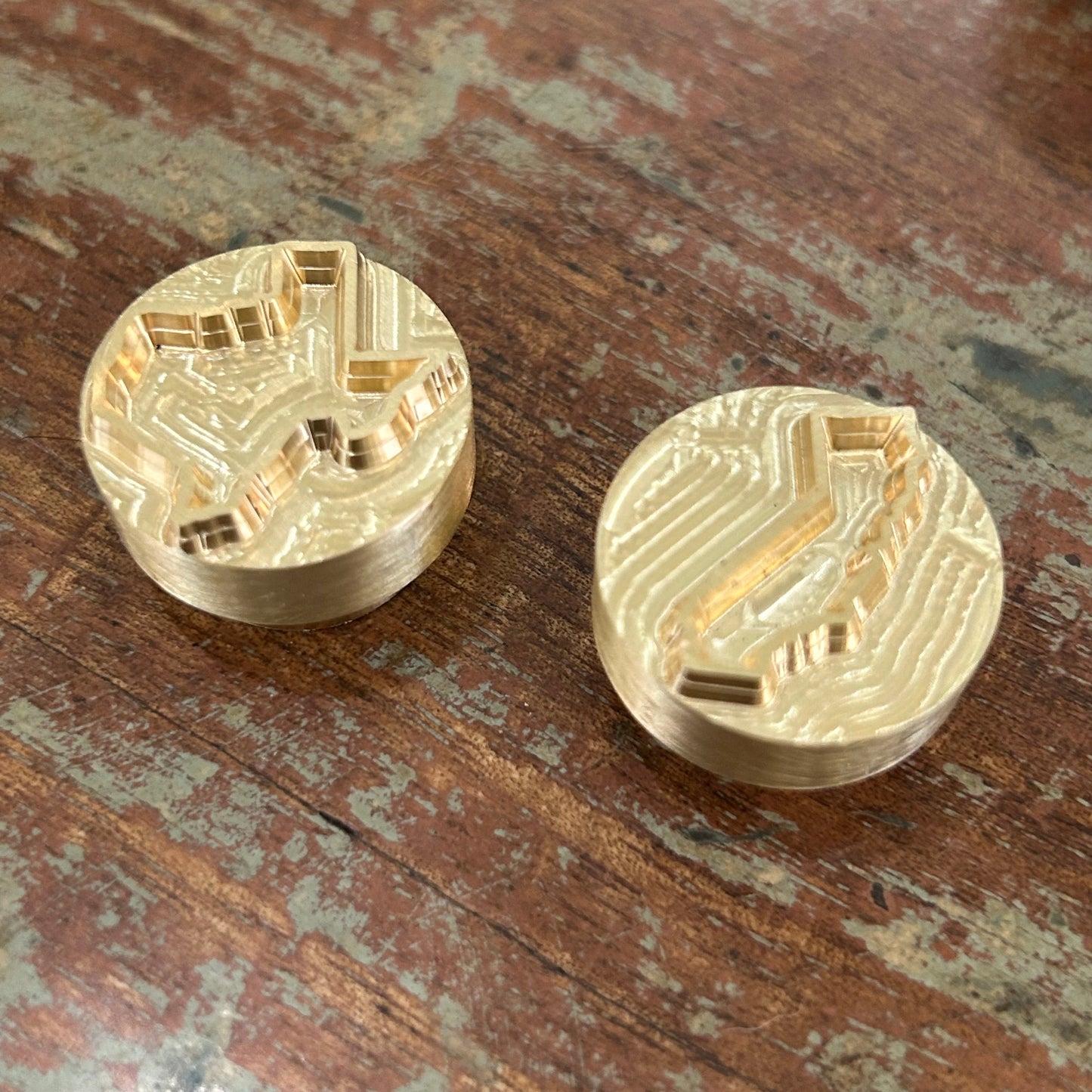 Two mini branding irons with brass heads, one with a Kentucky state silhouette and the other with a California design, displayed on a wooden surface.