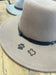 A close-up of a cowboy hat featuring custom miniature branding iron marks in the shape of a paw and a state outline.